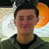 Young man smiling at the camera with orange and white balloons in the background at a party venue.