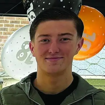 Young man smiling at the camera with orange and white balloons in the background at a party venue.