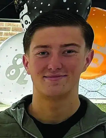 Young man smiling at the camera with orange and white balloons in the background at a party venue.