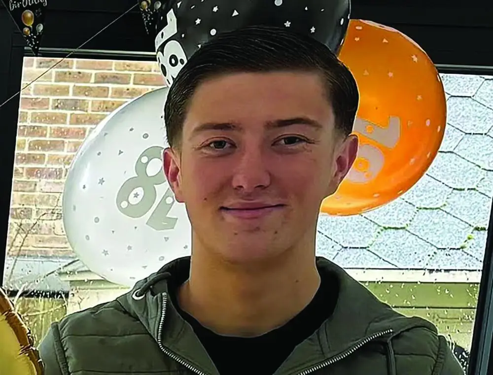 Young man smiling at the camera with orange and white balloons in the background at a party venue.
