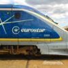 Blue Eurostar high-speed train side with white logo and branding, at a station platform with people in the background.