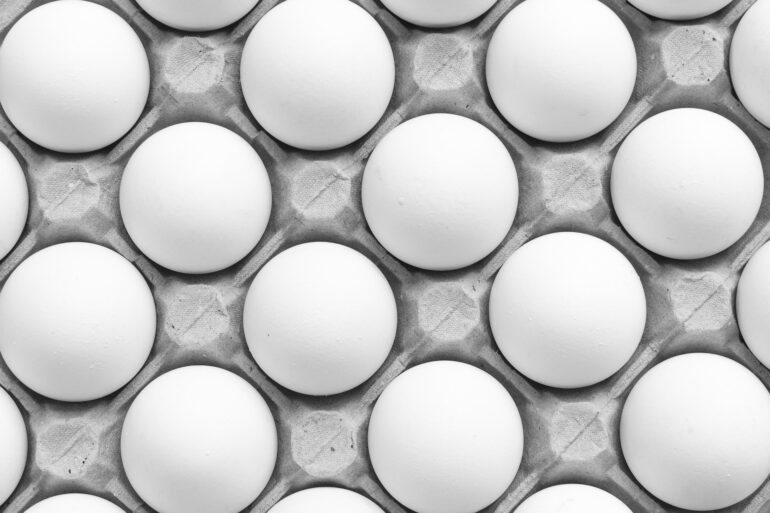 Close-up of white eggs neatly arranged in a gray egg carton in grayscale.