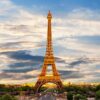 Eiffel Tower illuminated in warm gold rises over a Paris cityscape at sunset.