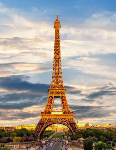Eiffel Tower illuminated in warm gold rises over a Paris cityscape at sunset.