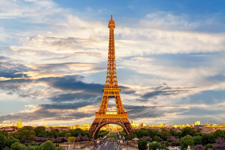 Eiffel Tower illuminated in warm gold rises over a Paris cityscape at sunset.