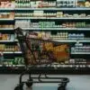 Shopping cart filled with groceries in a supermarket aisle full of shelves behind it