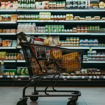 Shopping cart filled with groceries in a supermarket aisle full of shelves behind it