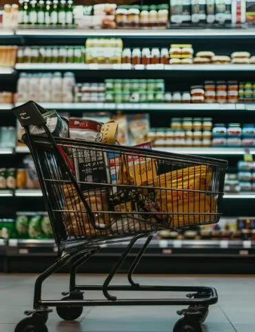 Shopping cart filled with groceries in a supermarket aisle full of shelves behind it