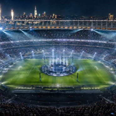 Nighttime stadium concert with a circular stage at the center, fireworks, and a packed crowd surrounding the field.