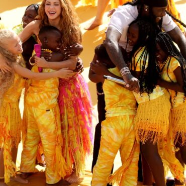 Group of smiling people in yellow outfits hugging in a sunny outdoor event, celebrating together.