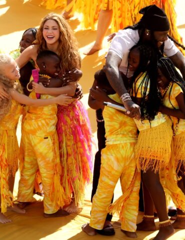 Group of smiling people in yellow outfits hugging in a sunny outdoor event, celebrating together.