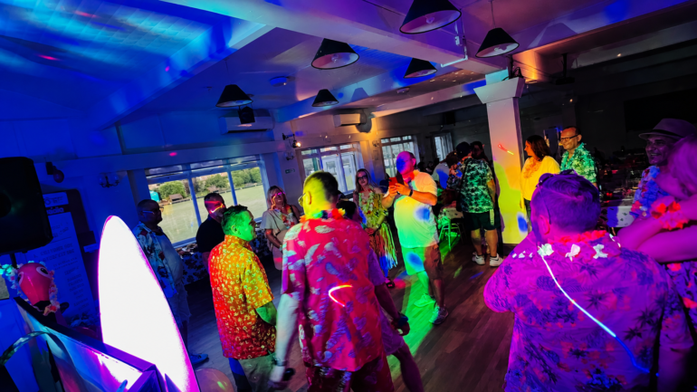 Aloha party - NOTE.radio - Polskie radio w UK | Polskie radio w Londynie People dancing at a colorful party with neon lights, wearing Hawaiian shirts and leis in a bright, festive venue