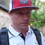 Man outdoors wearing a red Alfa Romeo cap and white polo shirt with a backpack over the shoulders