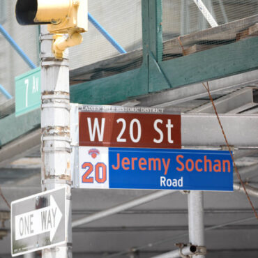 Intersection sign cluster: W 20 St and Jeremy Sochan Road with a One Way sign and construction scaffolding in the background.