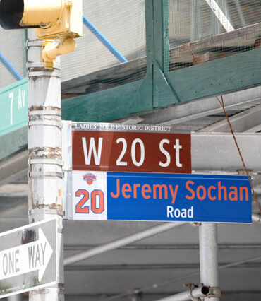 Intersection sign cluster: W 20 St and Jeremy Sochan Road with a One Way sign and construction scaffolding in the background.