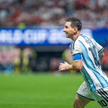 Soccer player in light blue and white striped jersey (number 10) runs on the field with a captain's armband during a match.