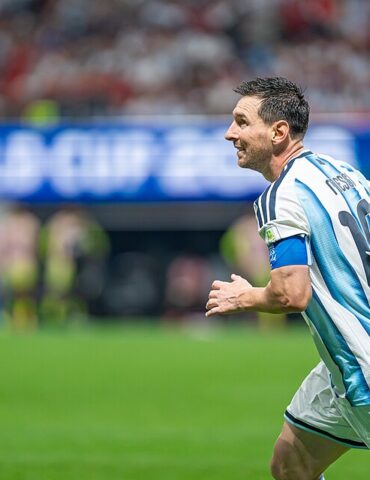 Soccer player in light blue and white striped jersey (number 10) runs on the field with a captain's armband during a match.