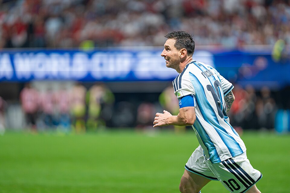 Soccer player in light blue and white striped jersey (number 10) runs on the field with a captain's armband during a match.