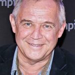 Smiling older man with short gray hair, wearing a blue striped shirt and dark blazer, close-cropped portrait.