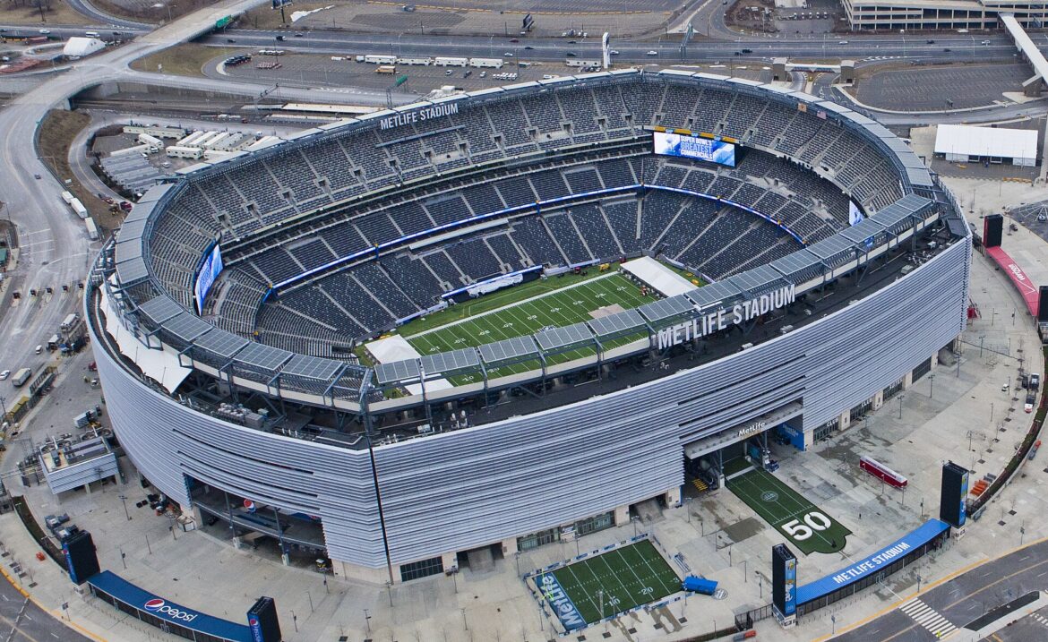 Aerial view of MetLife Stadium with a football field inside the bowl and surrounding seating and structures outside the arena.