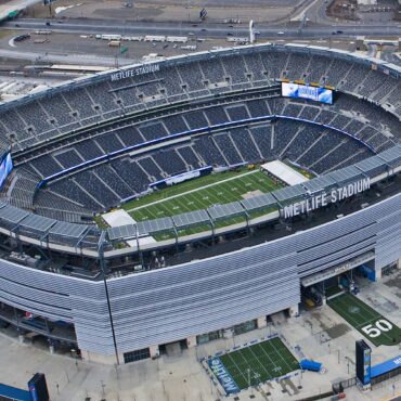 Aerial view of MetLife Stadium with a football field inside the bowl and surrounding seating and structures outside the arena.