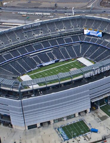 Aerial view of MetLife Stadium with a football field inside the bowl and surrounding seating and structures outside the arena.