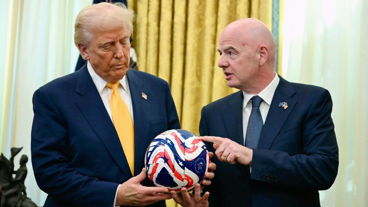 Two men in dark suits hold a red, white, and blue star-spangled ball indoors, one touching it as they discuss it.