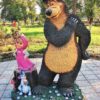 Large bear statue in a park with a small girl statue in a pink hood and a rabbit nearby on a flowered pedestal.