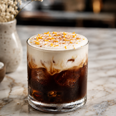 Glass of iced coffee with creamy foam and orange zest sprinkles on a marble surface