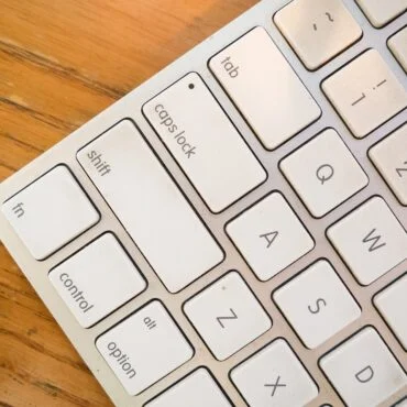 Close-up of a white keyboard on a wooden desk, showing keys such as Caps Lock, Tab, Shift, Control, and letter keys A, W, S, Z.