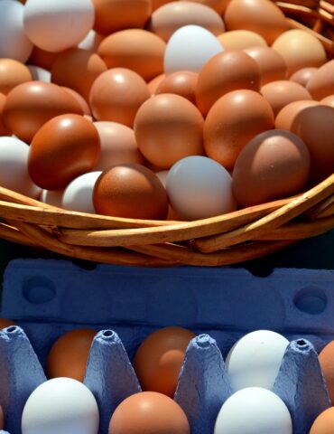 Basket of brown and white eggs in a woven basket on a blue egg carton nearby.