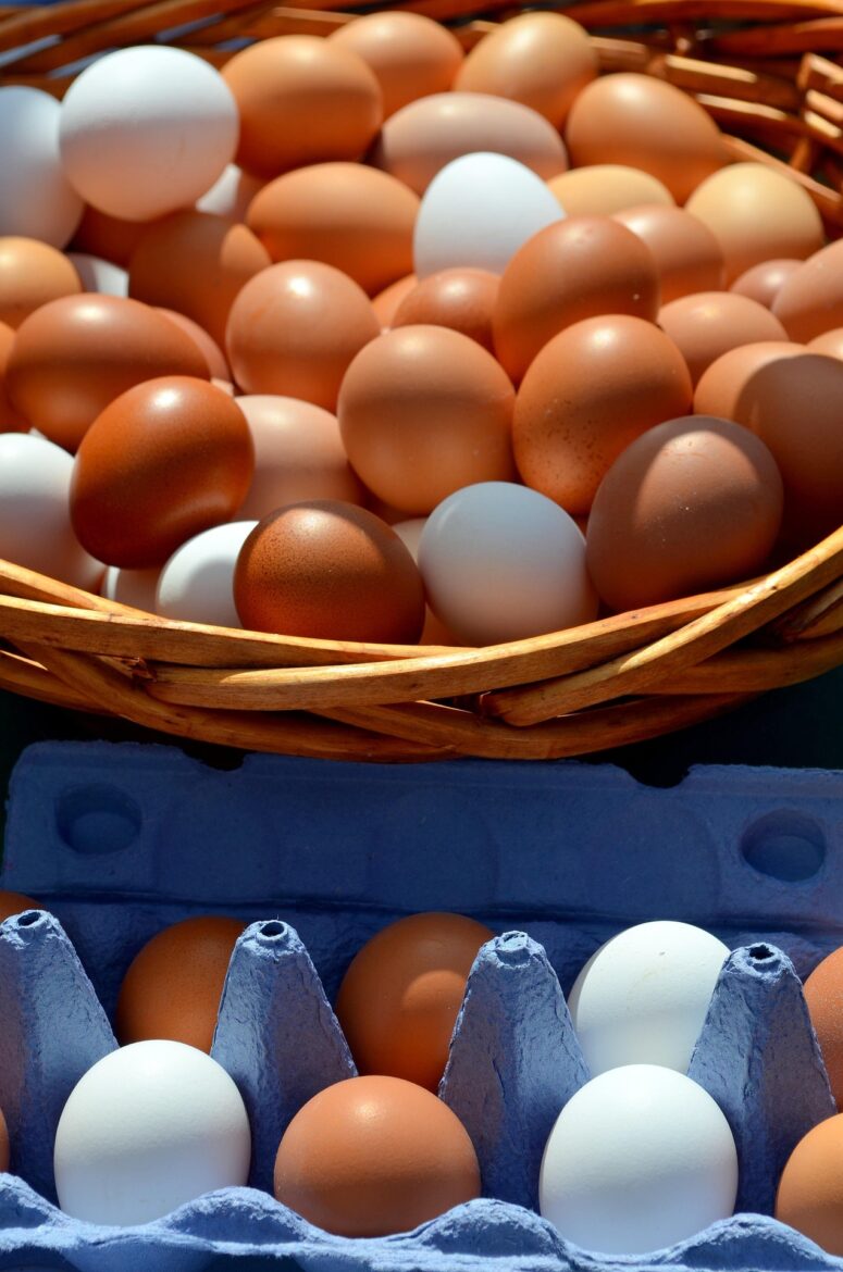 Basket of brown and white eggs in a woven basket on a blue egg carton nearby.