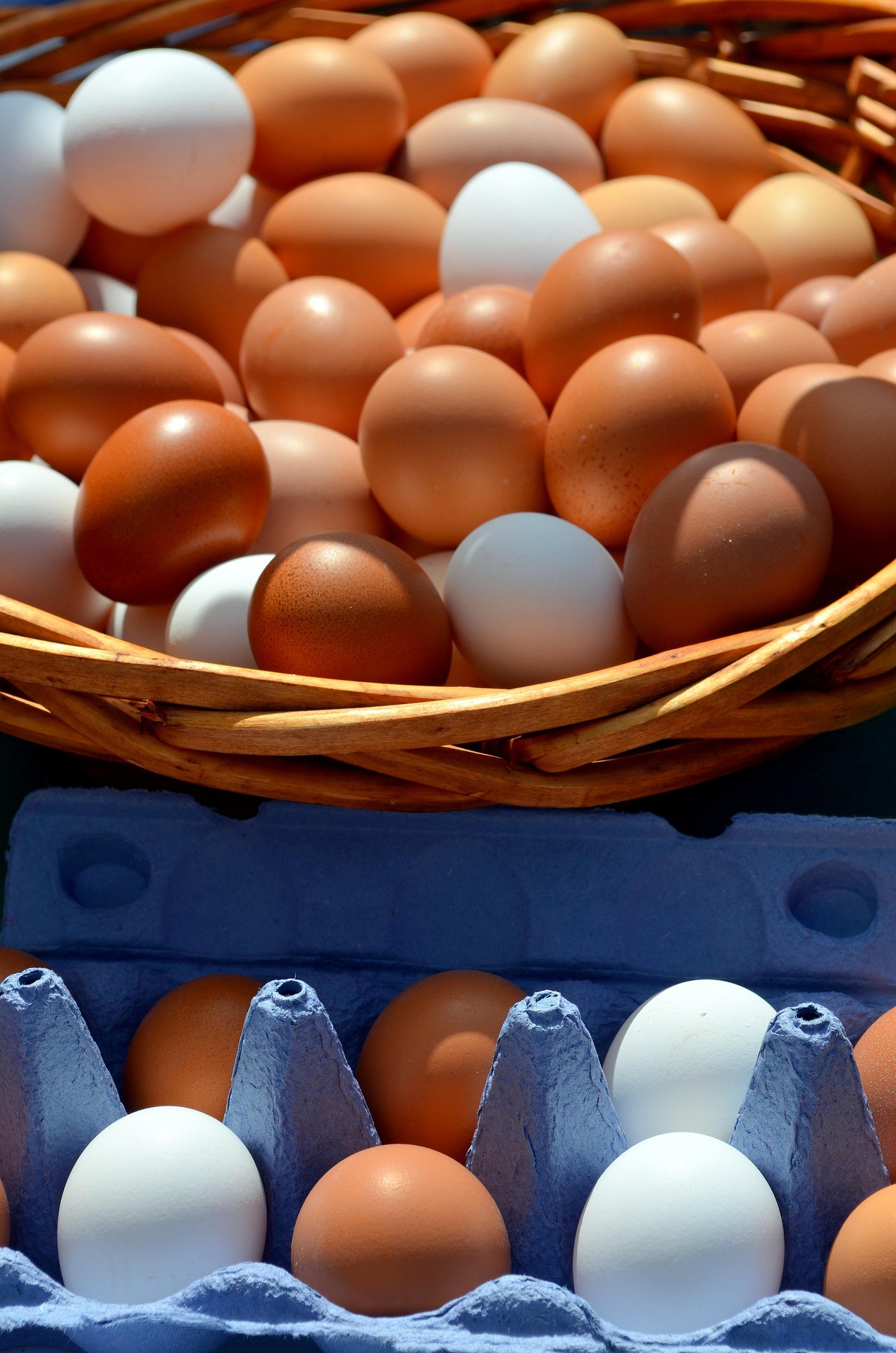 Basket of brown and white eggs in a woven basket on a blue egg carton nearby.