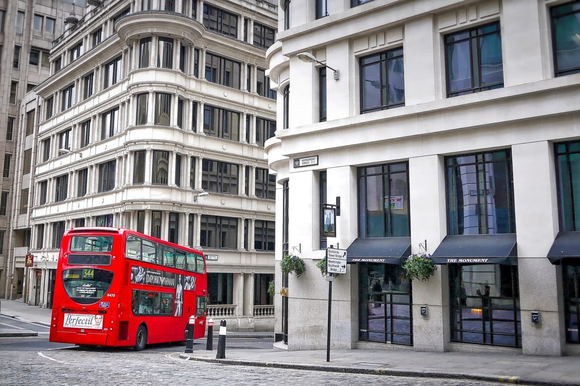 Red double-decker bus on a cobblestone street beside white curved-edge buildings with tall windows in a cityscape