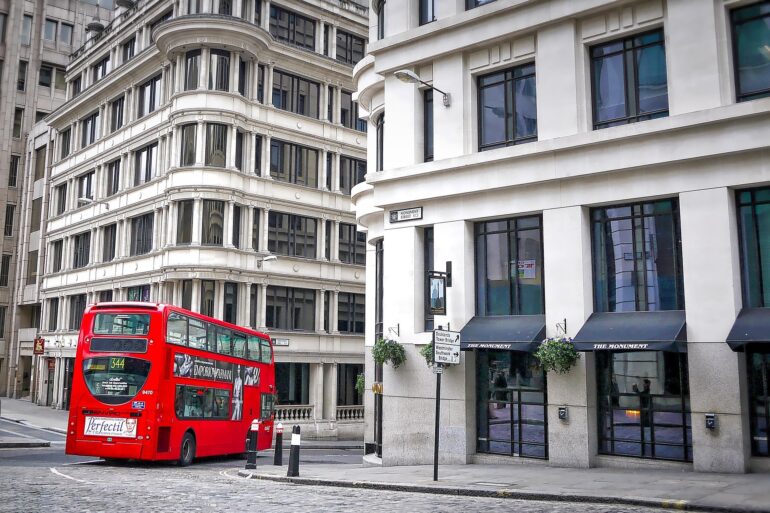 Red double-decker bus on a cobblestone street beside white curved-edge buildings with tall windows in a cityscape