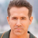 Ryan Reynolds - NOTE.radio - Polskie radio w UK | Polskie radio w Londynie Close-up of a man with short brown hair and a neutral expression, outdoors with a blurred urban background.