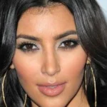 Close-up portrait of a woman with dark hair, bold eye makeup, and large gold hoop earrings, facing the camera.