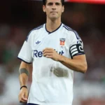 Álvaro Morata - NOTE.radio - Polskie radio w UK | Polskie radio w Londynie Male soccer player in a white jersey with a captain's armband on his left arm, standing on the field.
