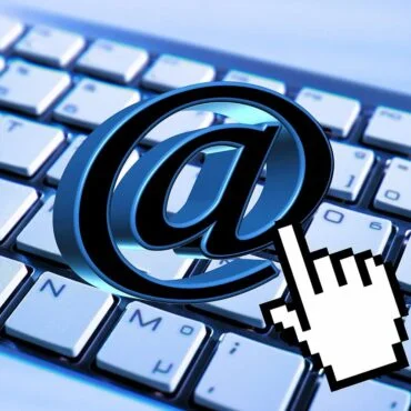 Large blue '@' symbol on a computer keyboard with a pixelated hand cursor pointing at it, signaling internet or email access