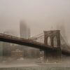 Brooklyn Bridge with its towers and cables fading into a foggy NYC skyline across the river.