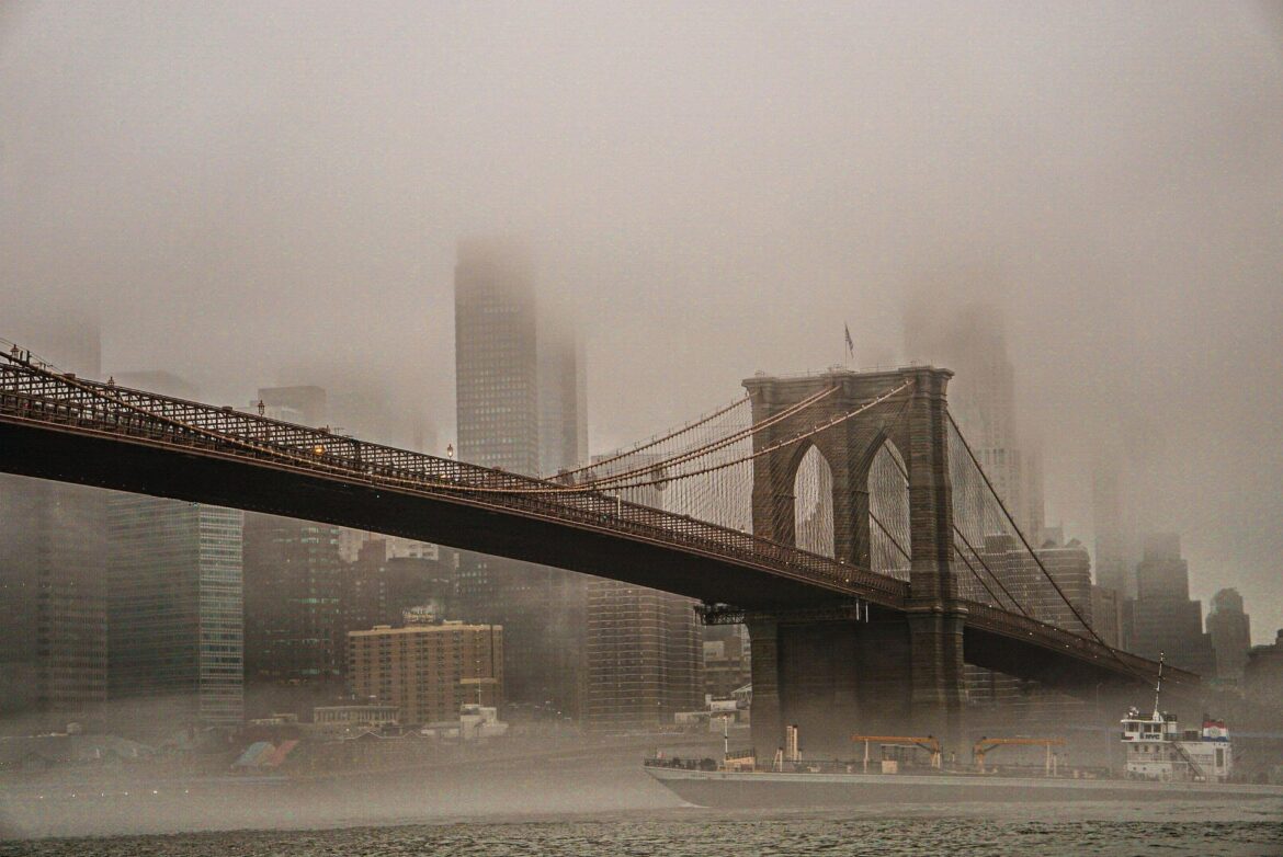 Brooklyn Bridge with its towers and cables fading into a foggy NYC skyline across the river.