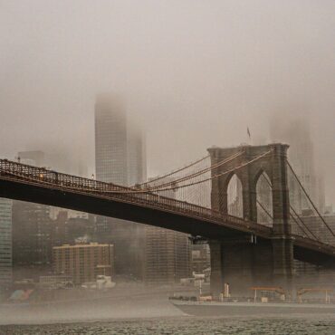 Brooklyn Bridge with its towers and cables fading into a foggy NYC skyline across the river.