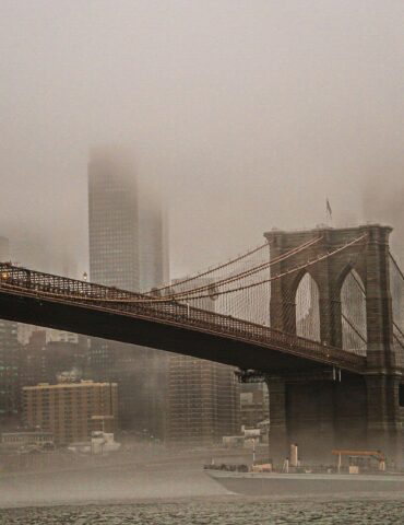 Brooklyn Bridge with its towers and cables fading into a foggy NYC skyline across the river.
