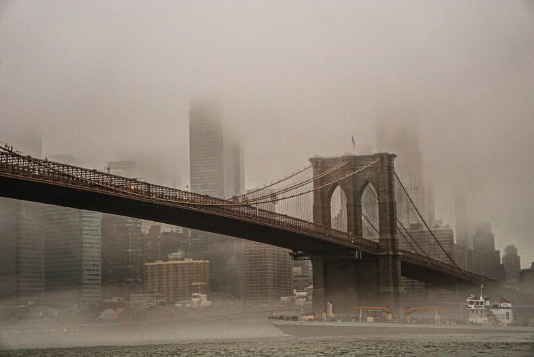 NOWY JORK - NOTE.radio - Polskie radio w UK | Polskie radio w Londynie Brooklyn Bridge with its towers and cables fading into a foggy NYC skyline across the river.
