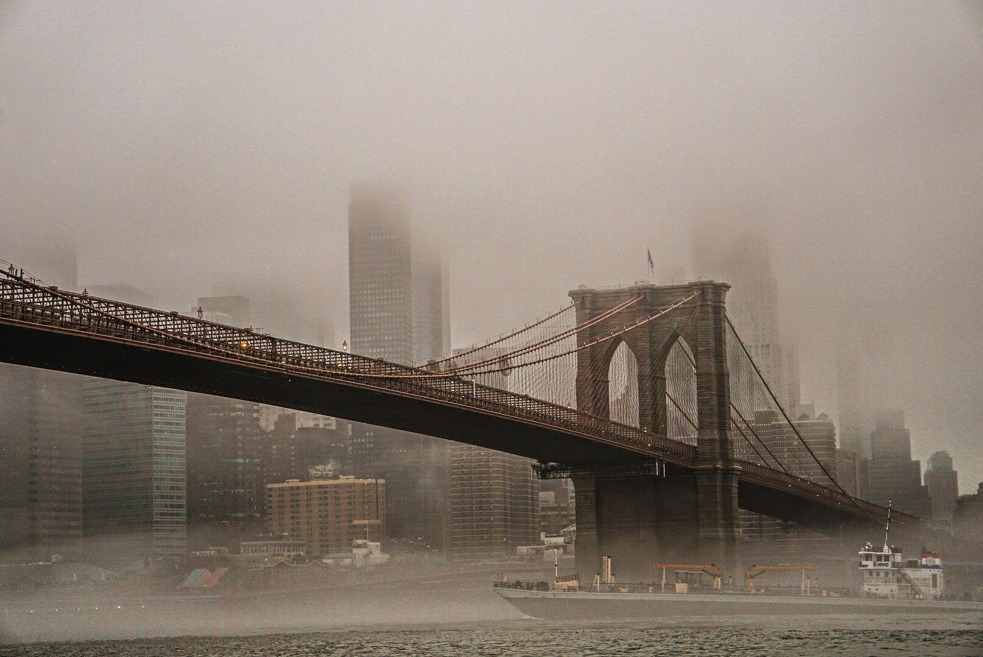 Brooklyn Bridge with its towers and cables fading into a foggy NYC skyline across the river.