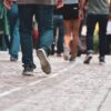 People walking away from the camera on a cobblestone sidewalk beside water, viewed from behind.