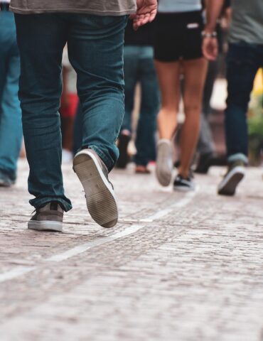 People walking away from the camera on a cobblestone sidewalk beside water, viewed from behind.