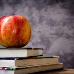 Red and yellow apple resting on top of a stack of closed books on a wooden table.