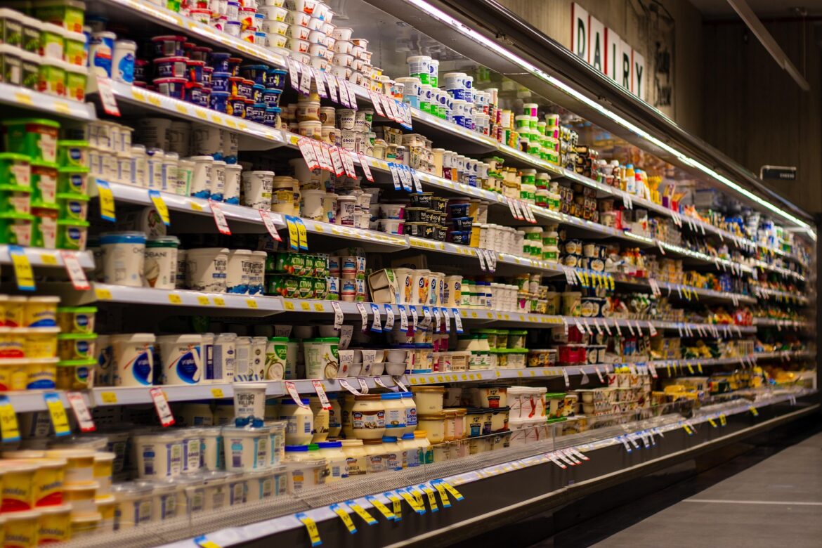 Aisle in a grocery store's refrigerated dairy section filled with yogurt cups and tubs on shelves.