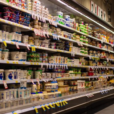 Aisle in a grocery store's refrigerated dairy section filled with yogurt cups and tubs on shelves.